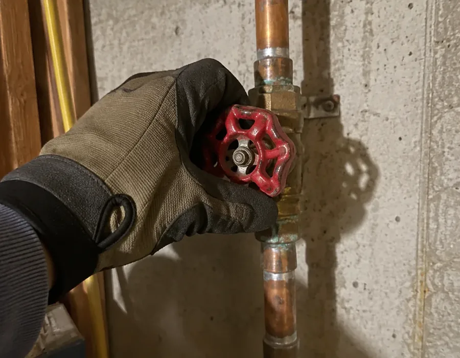 Hand turning an emergency water shutoff valve in a basement