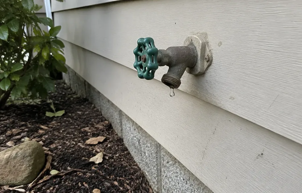 Outdoor hose faucet with drip at the spout beside Chelmsford siding
