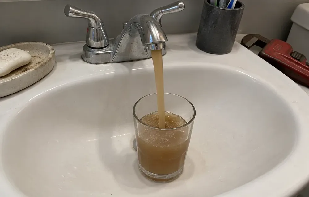 Brown tap water filling a clear glass beside a bathroom sink in Chelmsford